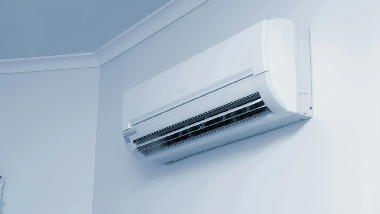 White wall-mounted indoor air conditioning unit on a pale blue wall