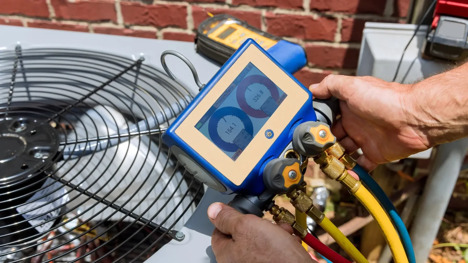 Digital refrigerant manifold and connected hoses beside an outdoor air conditioning unit