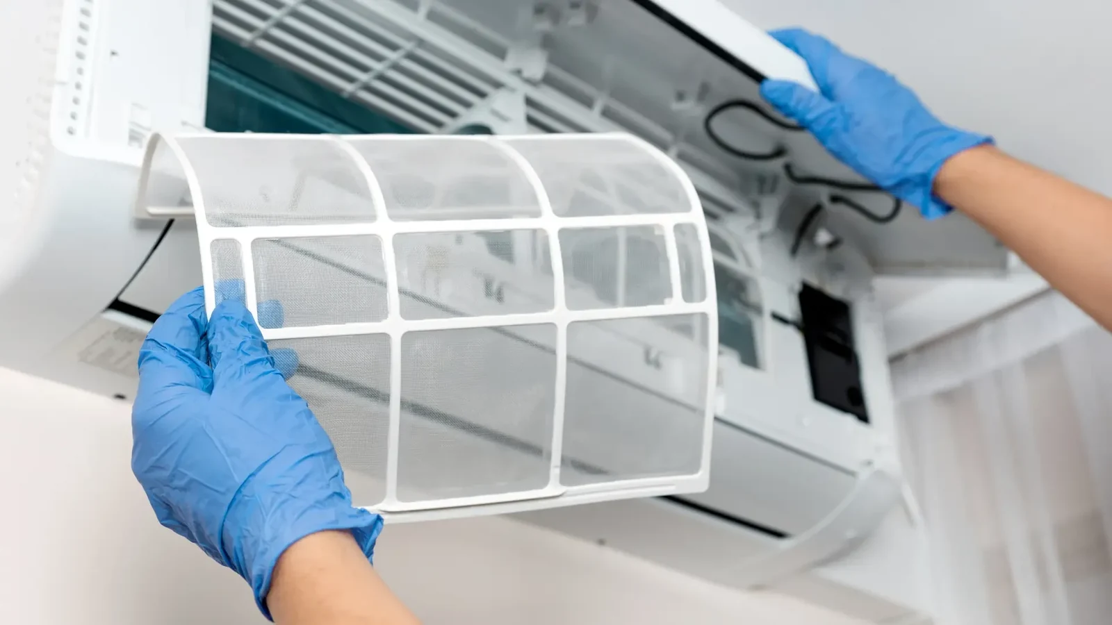 Gloved hands removing the mesh filter from an indoor air conditioning unit for servicing