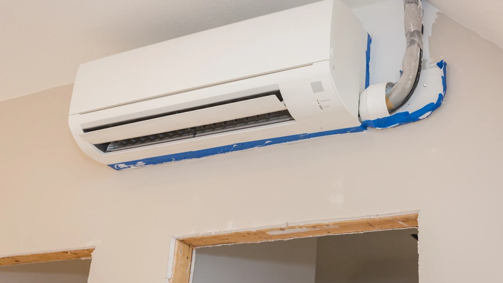 Indoor split air conditioning unit with exposed insulated pipework and protective blue tape during installation